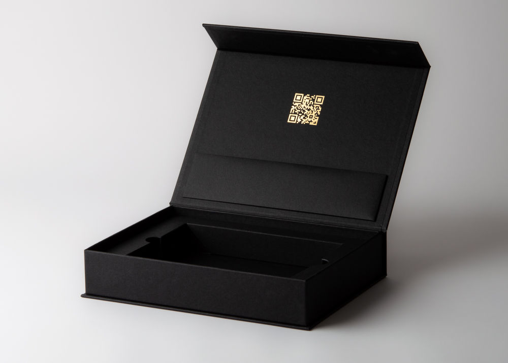 Geöffnete schwarze Musterbox mit Forminlay und goldenem QR-Code im Deckel