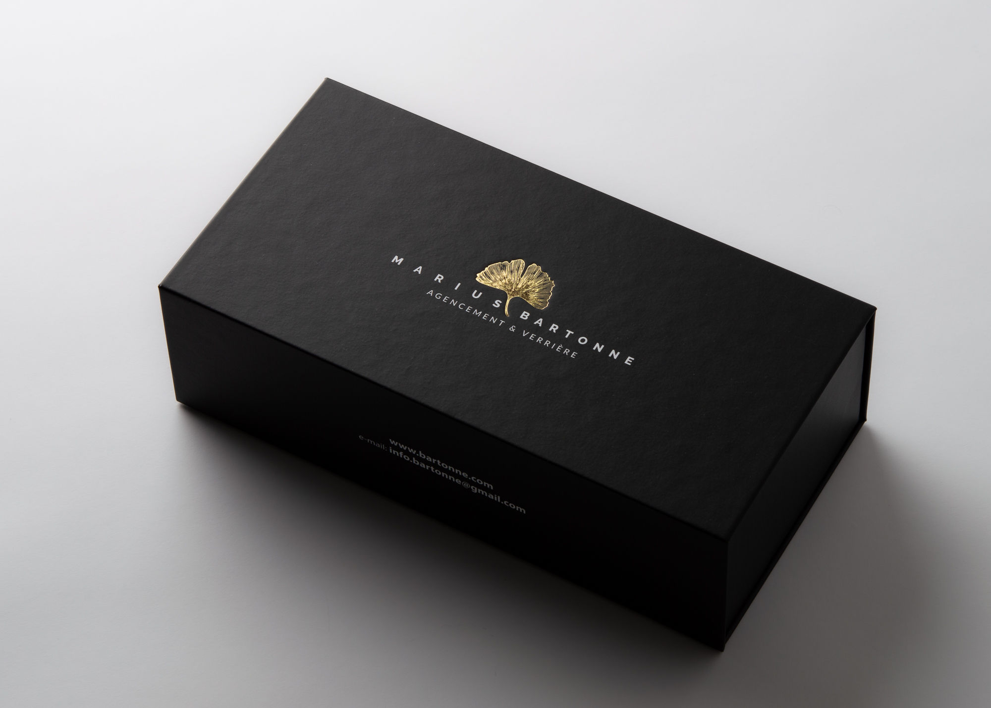 Geschlossene schwarze Präsentationsbox mit weißem Schriftzug und goldenem Blütenmotiv