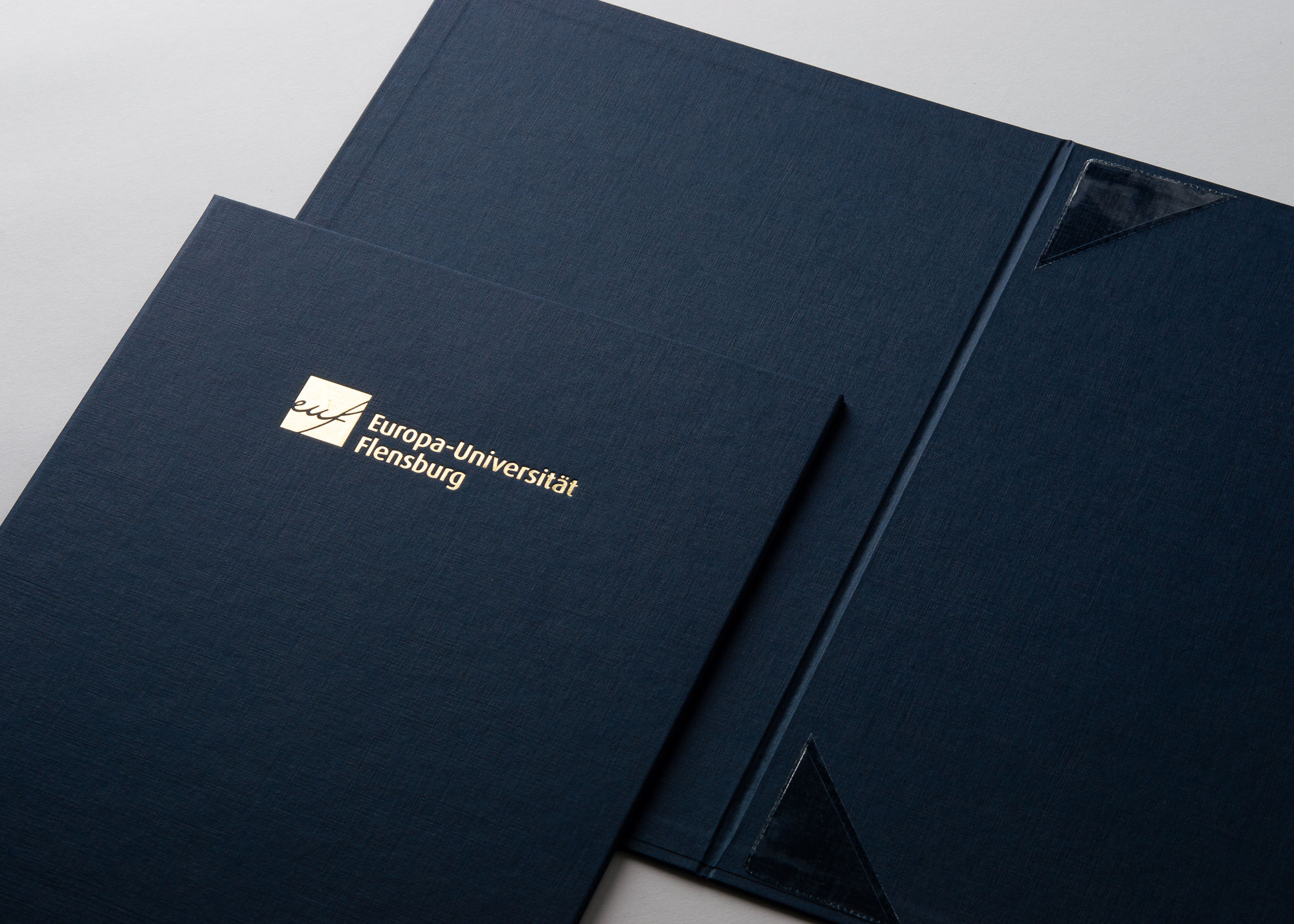 Dunkelblaue Urkundenmappen mit goldgeprägtem Universitätslogo und transparenten Ecktaschen